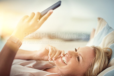Buy stock photo Shot of a mature woman reading a text message while relaxing on the sofa at home