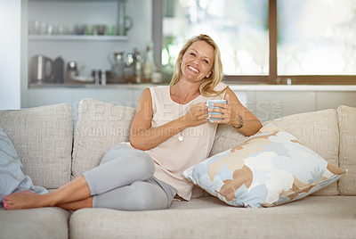 Buy stock photo Portrait of a mature woman enjoying a warm beverage while relaxing on the sofa at home
