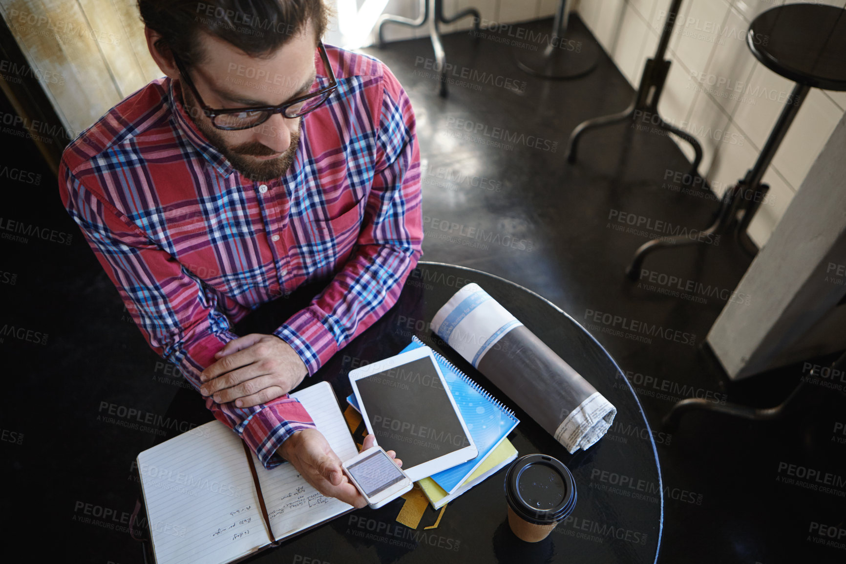 Buy stock photo Shot of a young man sitting at a table in a cafe with his cellphone, digital tablet and diary in front of him