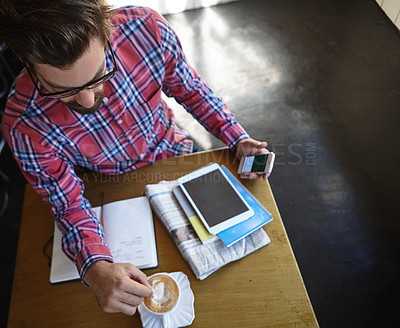 Buy stock photo Shot of a young man sitting at a table in a cafe with his cellphone, digital tablet and diary in front of him