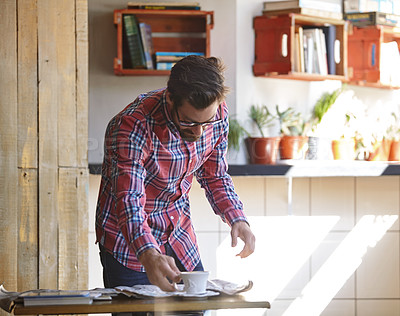 Buy stock photo Shot of a young man having coffee while reading the newspaper in a cafe