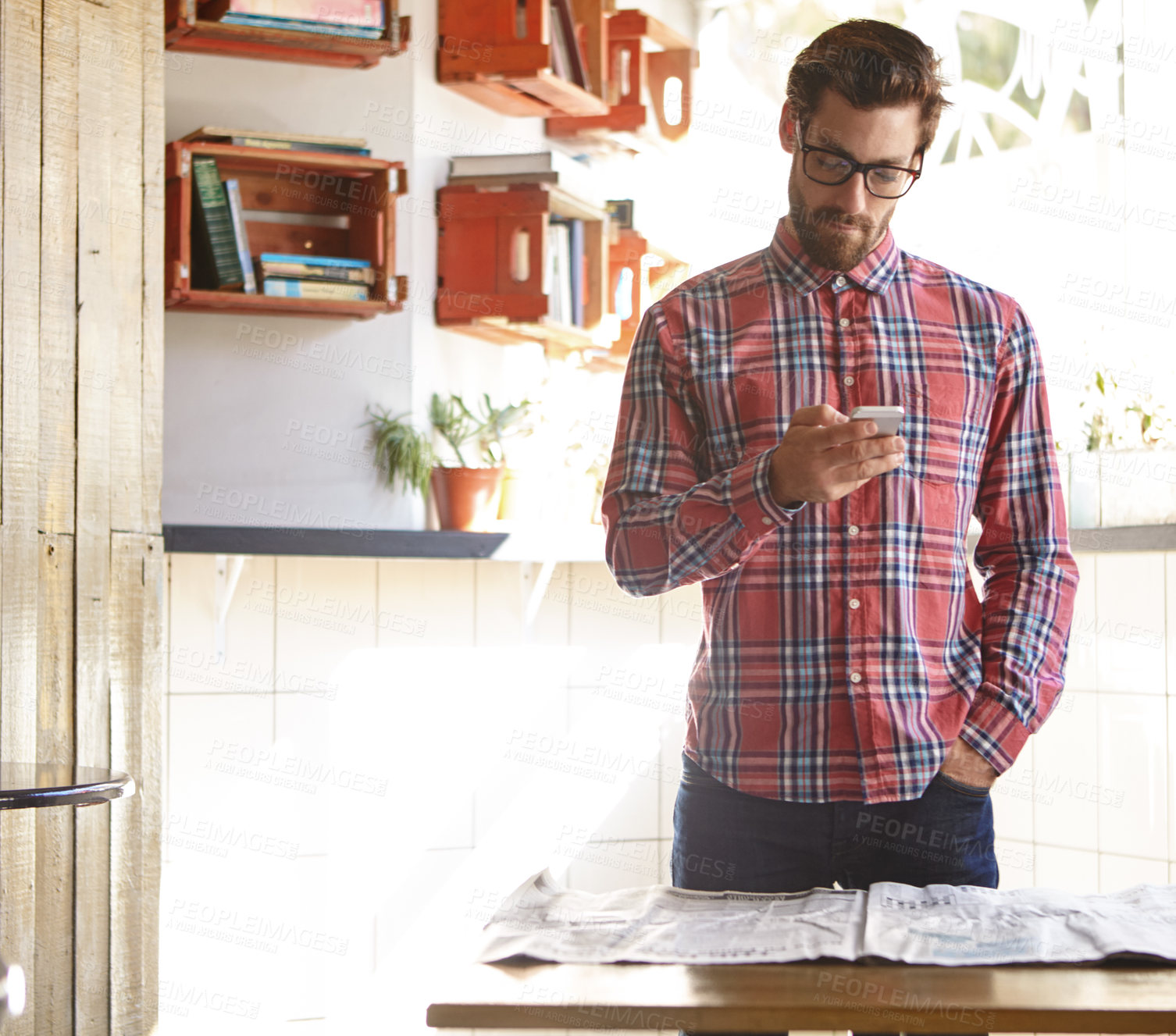 Buy stock photo Shot of a young man using his cellphone in a cafe with the newspaper lying in front of him