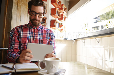 Buy stock photo Shot of a young man using his digital tablet while sitting in a cafe