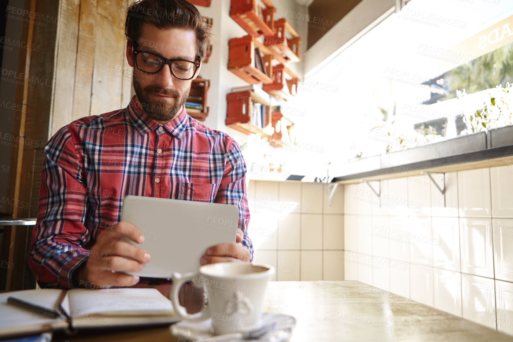 Buy stock photo Shot of a young man using his digital tablet while sitting in a cafe