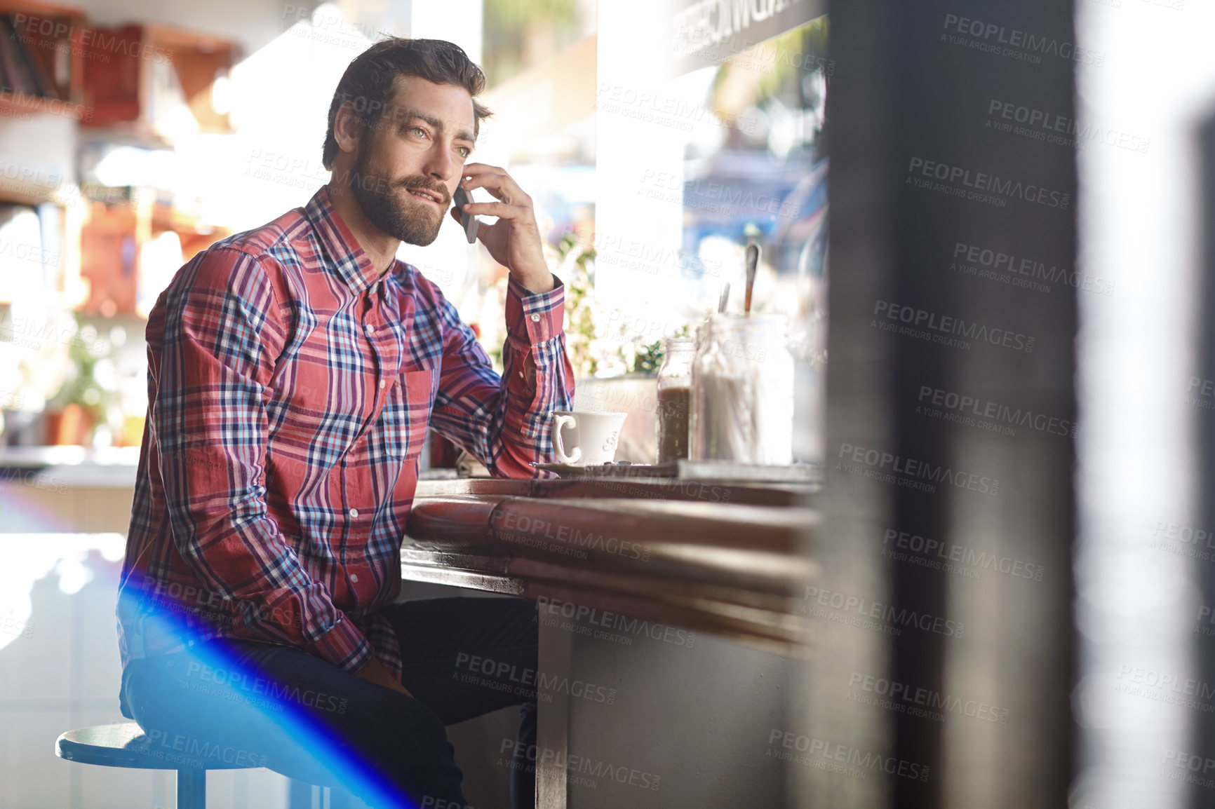 Buy stock photo Shot of a young man talking on his cellphone while sitting in a cafe