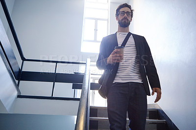 Buy stock photo Cropped shot of a young man walking down a staircase holding a coffee