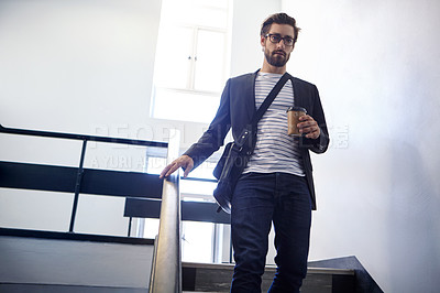 Buy stock photo Cropped shot of a young man walking down a staircase holding a coffee