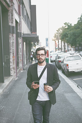 Buy stock photo Shot of a stylish young man using a cellphone while walking in the city
