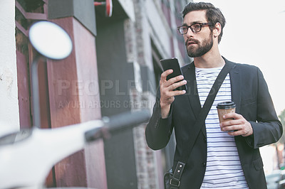 Buy stock photo Shot of a stylish young man using a cellphone while walking in the city