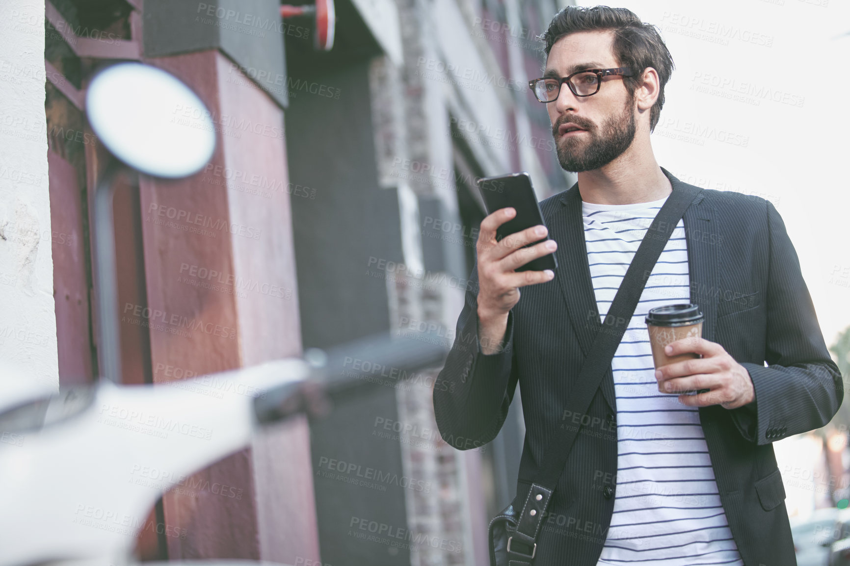 Buy stock photo Shot of a stylish young man using a cellphone while walking in the city