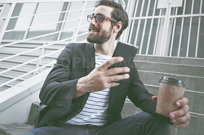 Buy stock photo A stylish young man sitting with his cellphone and a takeaway coffee in the city