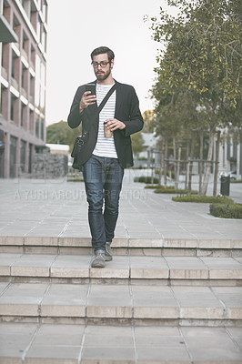 Buy stock photo Shot of a stylish young man using a cellphone while out walking in the city
