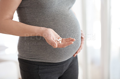 Buy stock photo Cropped shot of a pregnant woman holding tablets while standing in her home