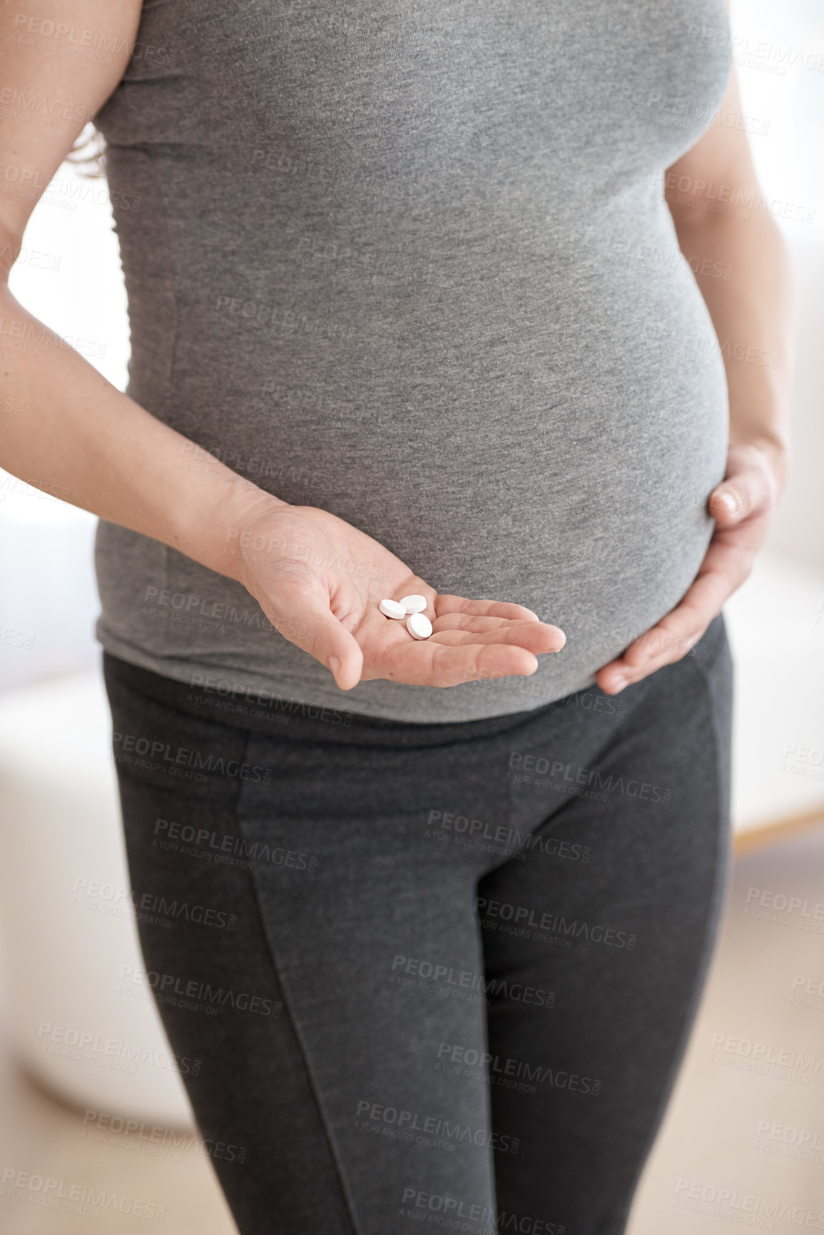 Buy stock photo Cropped shot of a pregnant woman holding tablets while standing in her home