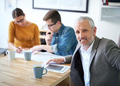 Buy stock photo Portrait of a mature businessman with his colleagues working in the background