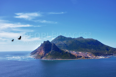 Buy stock photo Blue sky, birds and mountain or ocean with buildings in nature or fishing village by sea. Coastal town, clouds and waves or landscape in summer for travel, vacation and outdoor for holiday by beach