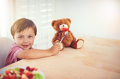 Buy stock photo Child, portrait and feeding fruit to teddy bear with fantasy play, imagination and watermelon for nutrition in dining room. Boy, kid and stuffed animal with breakfast bowl at lounge table for sharing