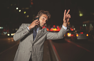 Buy stock photo A handsome businessman hailing a cab while talking on his cellphone in the city at night