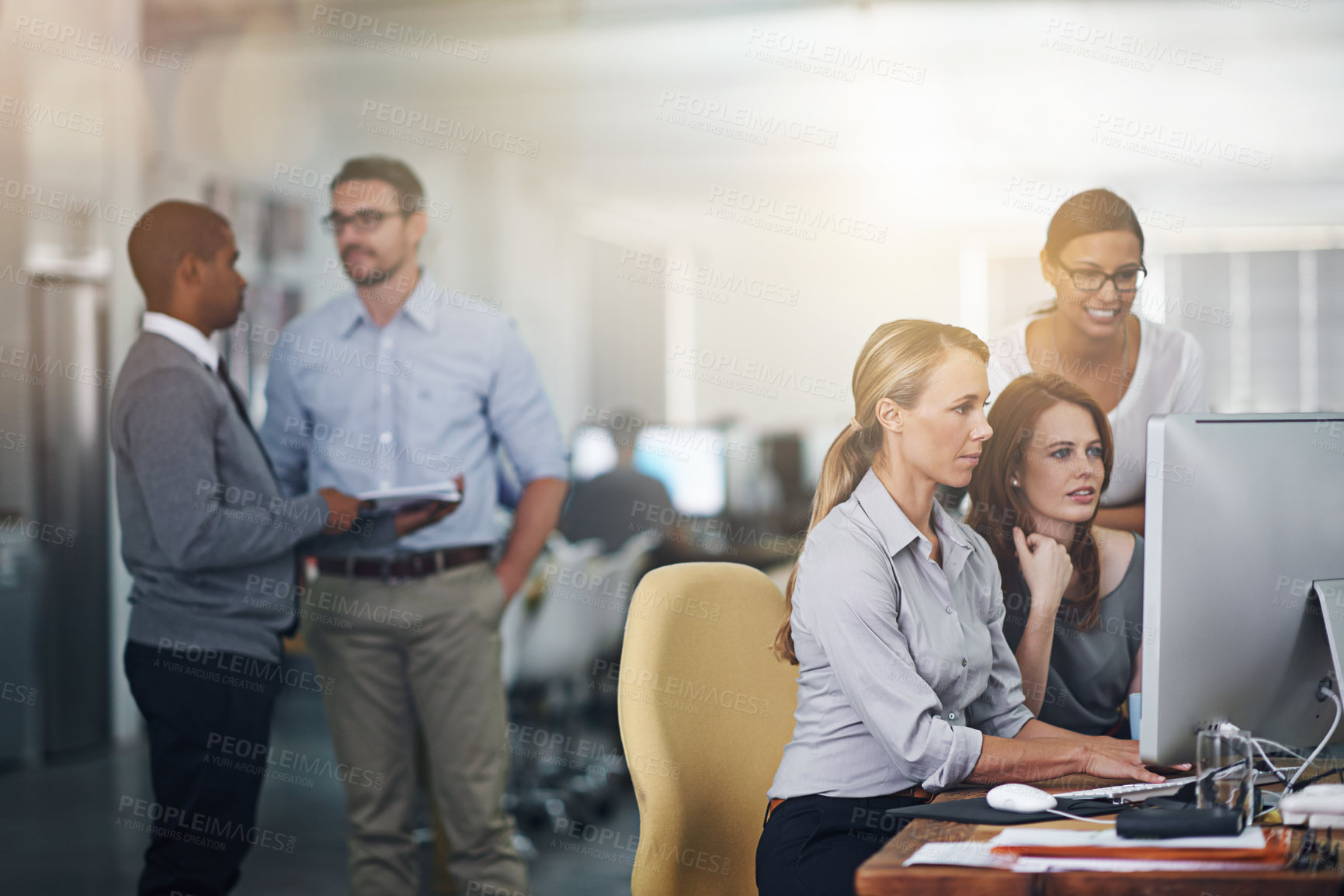 Buy stock photo Shot of three women working on a computer with colleagues blurred in the background