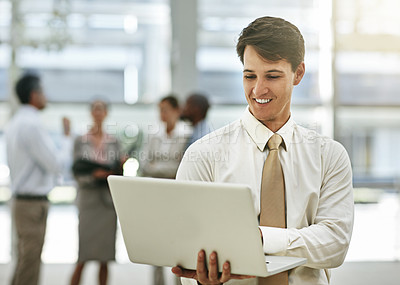 Buy stock photo Cropped shot of a young businessman using a laptop with his colleagues in the background