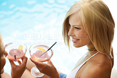 Buy stock photo Shot of two young friends drinking cocktails by the pool