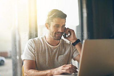 Buy stock photo A young man talking on the phone while sitting with his laptop in a coffee shop
