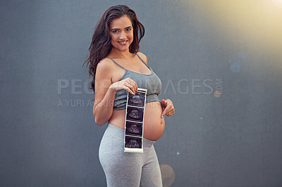 Buy stock photo Portrait of a pregnant woman holding her sonogram picture against a gray background