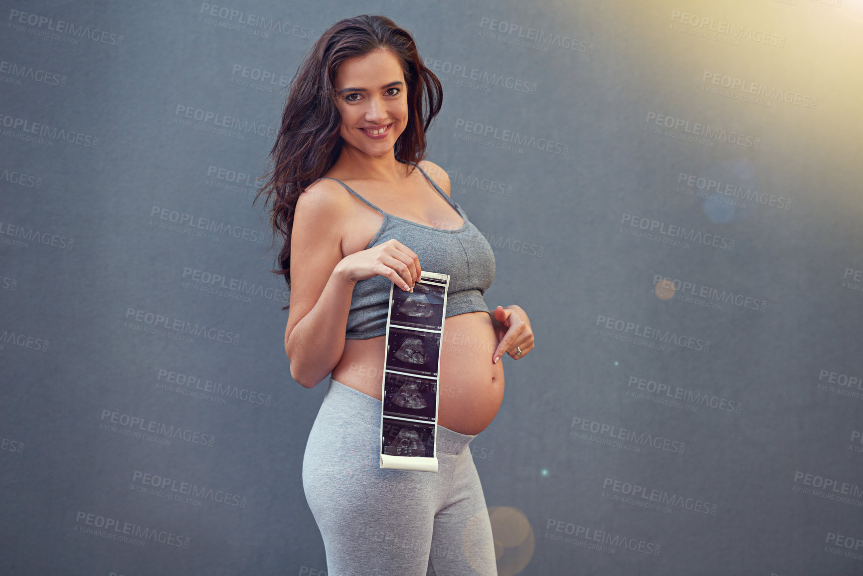 Buy stock photo Portrait of a pregnant woman holding her sonogram picture against a gray background