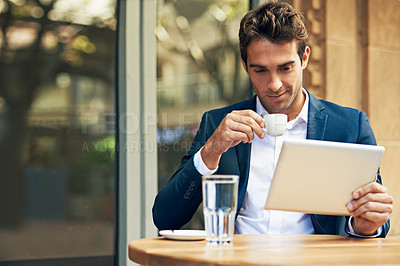 Buy stock photo A young businessman using his digital tablet while having coffee at an outdoor cafe