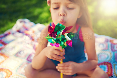 Buy stock photo Young girl, picnic and blowing pinwheel, garden and enjoying freedom of outside and happy. Colourful little child, backyard and summer for playing, toy and windmill for school holidays and happiness