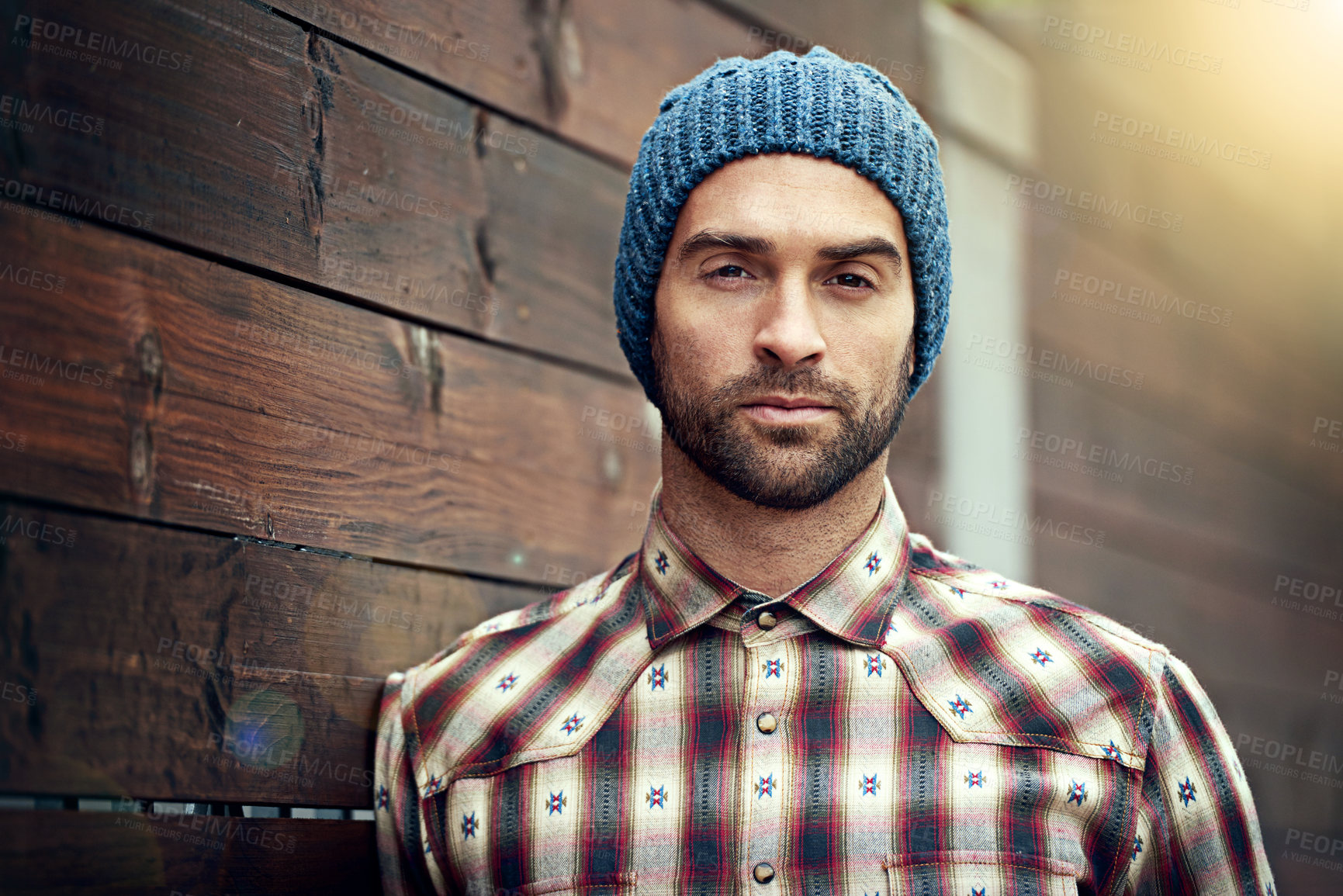 Buy stock photo Portrait, confident and man on wood wall background outdoor in casual clothes, outfit or apparel. Face, serious and stylish person in beanie, shirt and trendy fashion for profile picture in Spain