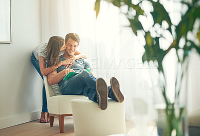 Buy stock photo Couple, embrace and read in house, love and chair to relax and hugging for learning and kiss. Man, woman and romance while happy, smile and book for entertainment and together in living room at home