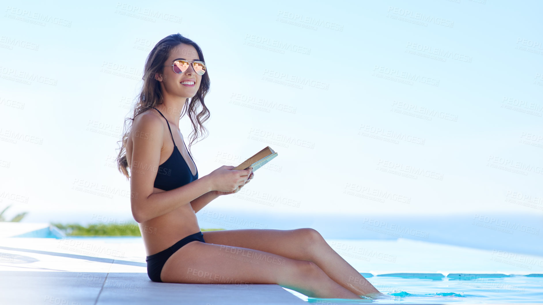 Buy stock photo Shot of a young woman reading a book by the poolside