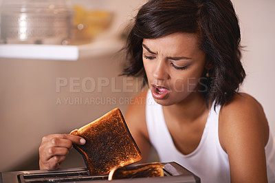 Buy stock photo Cropped shot of a young woman taking a piece of burnt toast from the toaster