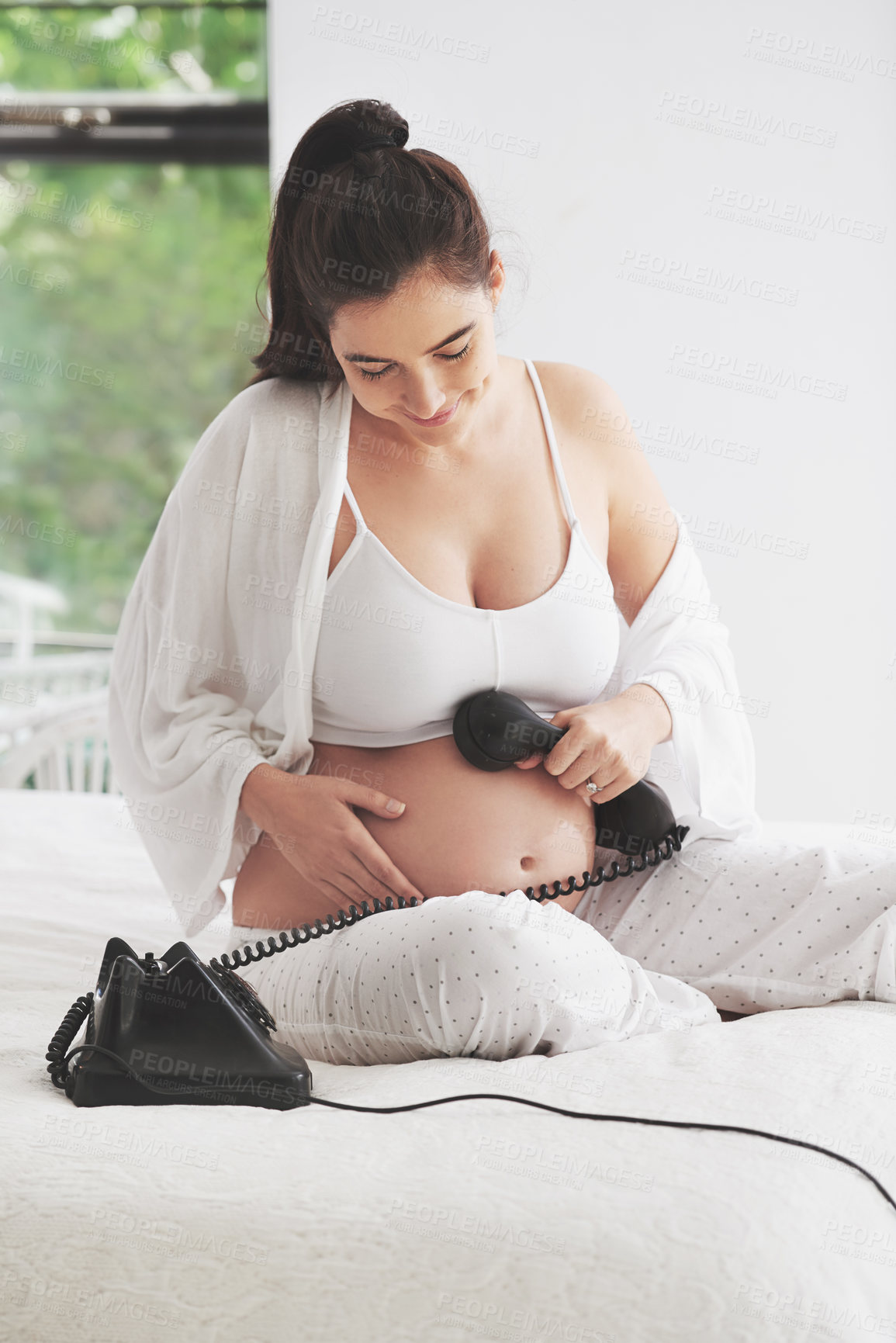 Buy stock photo Shot of a pregnant woman holding a telephone to her belly at home