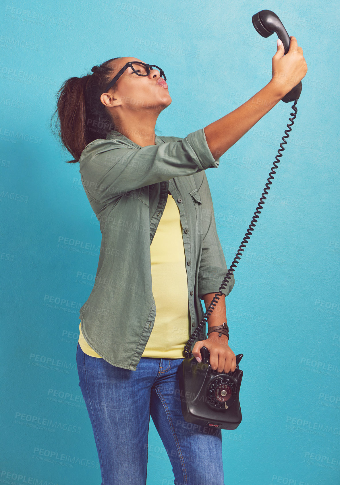 Buy stock photo Shot of a young woman talking a selfie on an old fashioned telephone