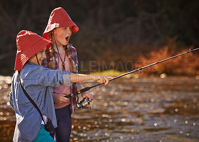 Buy stock photo Happy, young sisters and fishing in river or lake for relax, fun hobby and adventure outdoor in nature. Excited, girls or children and catching fish in water with bucket hat for recreation on holiday