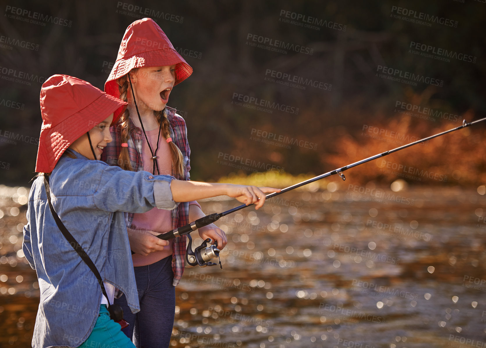 Buy stock photo Happy, young sisters and fishing in river or lake for relax, fun hobby and adventure outdoor in nature. Excited, girls or children and catching fish in water with bucket hat for recreation on holiday