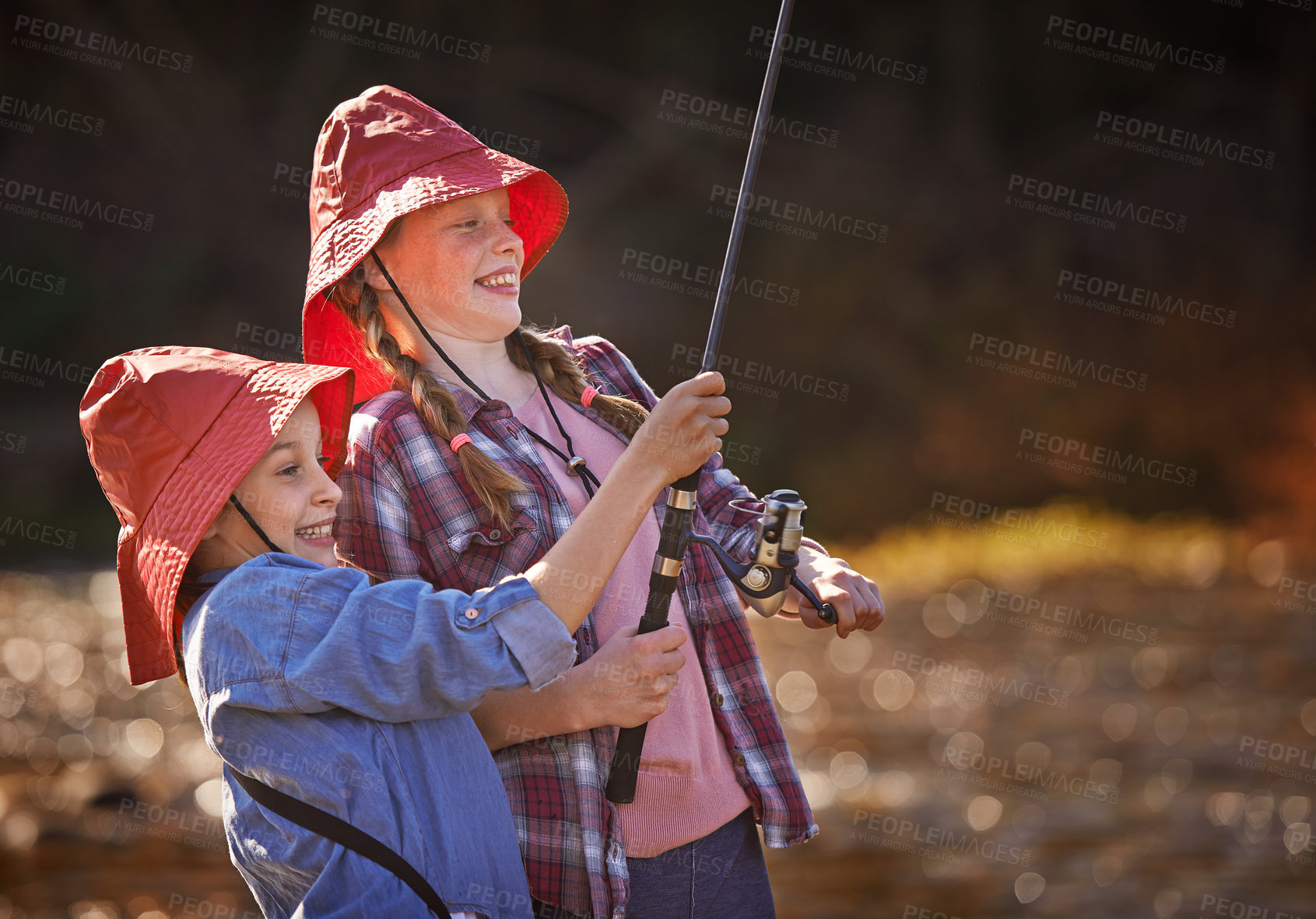 Buy stock photo Happy, young sisters and fishing together in river for relax, fun hobby and outdoor adventure in nature. Excited, girls or children and catching fish in lake with bucket hat for vacation activity