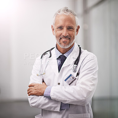 Buy stock photo Cropped portrait of a mature doctor standing with his arms folded in the hospital corridor