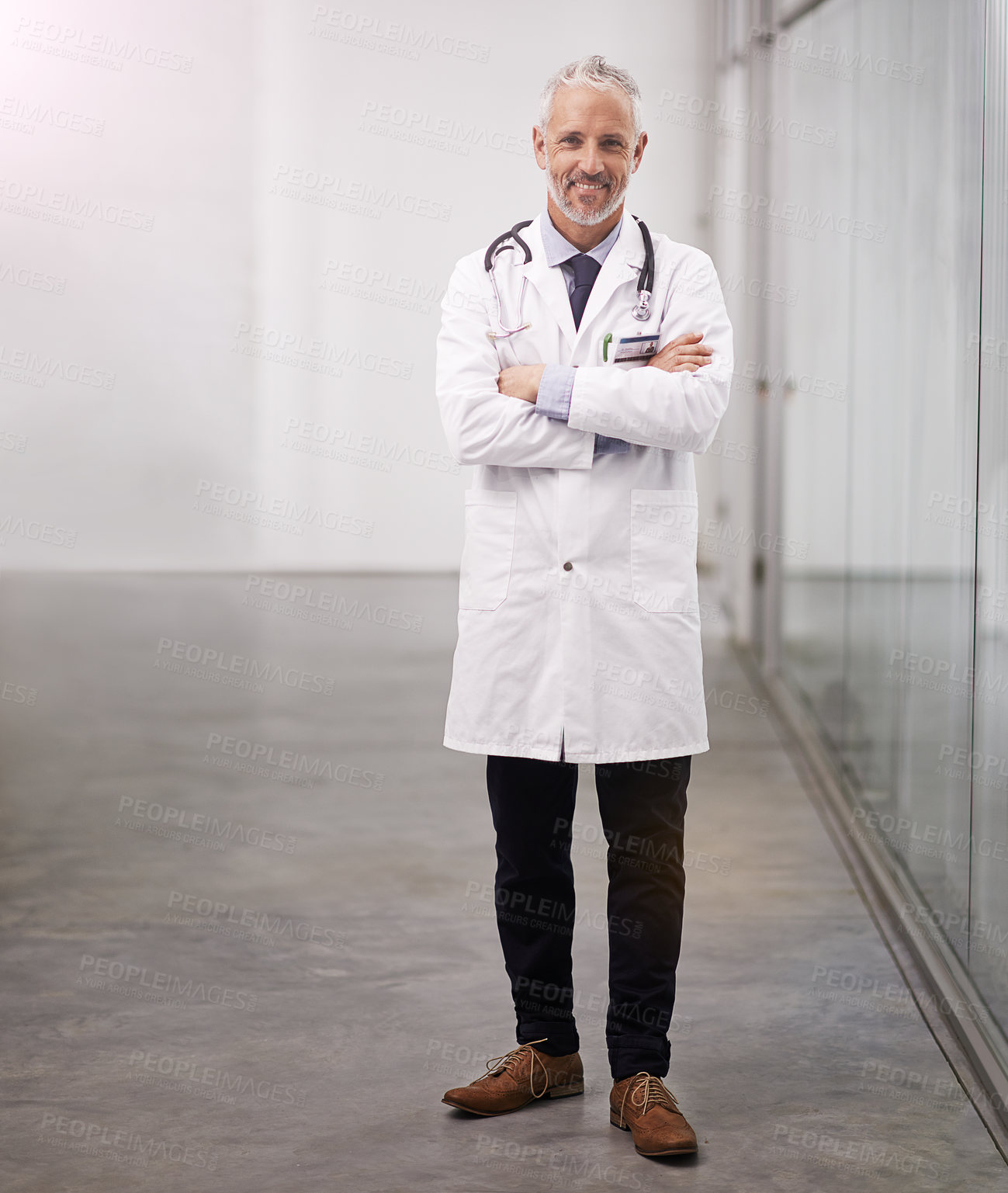 Buy stock photo Full length portrait of a mature doctor standing with his arms folded in the hospital corridor