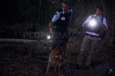 Buy stock photo Shot of two policemen and their canine tracking a suspect through the brush at night