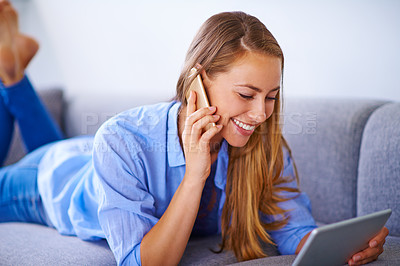 Buy stock photo A young woman making a phone call while looking at the screen of her digital tablet