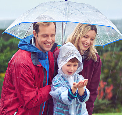 Buy stock photo Family, rain and umbrella outdoor in nature for fun, happiness and quality time with love. Man, woman and excited boy child with hands for water drops, learning and development while playing together