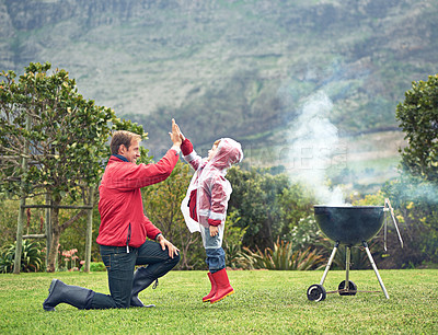 Buy stock photo Shot of a father giving his son a high five while they're having a barbecue outside