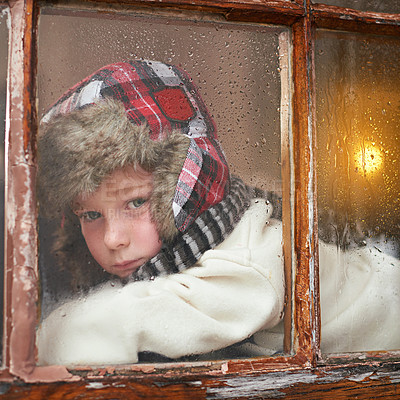 Buy stock photo A young boy lying by the window and looking bored while it rains outside