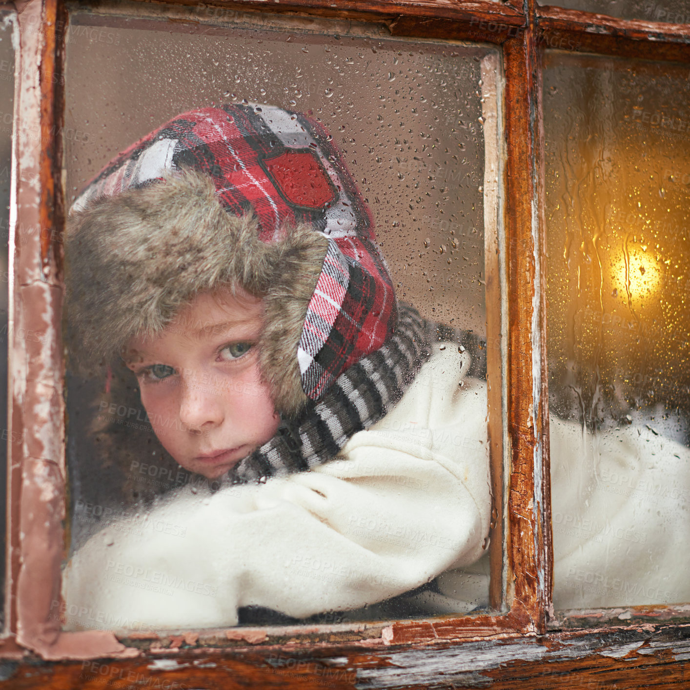 Buy stock photo A young boy lying by the window and looking bored while it rains outside