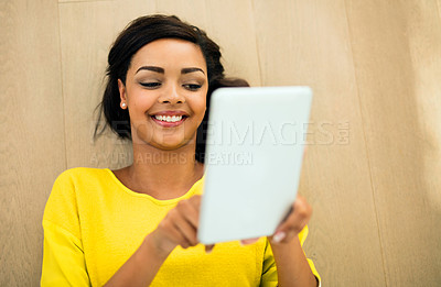 Buy stock photo High angle shot of a young woman using a digital tablet while lying on the floor at home