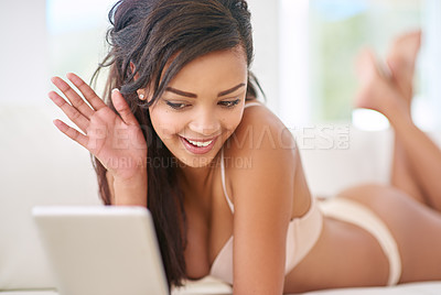 Buy stock photo Shot of a gorgeous young woman using her tablet while lying on the sofa in lingerie