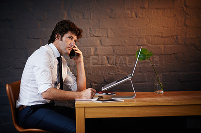 Buy stock photo Shot of a businessman talking on the phone while working late at the office